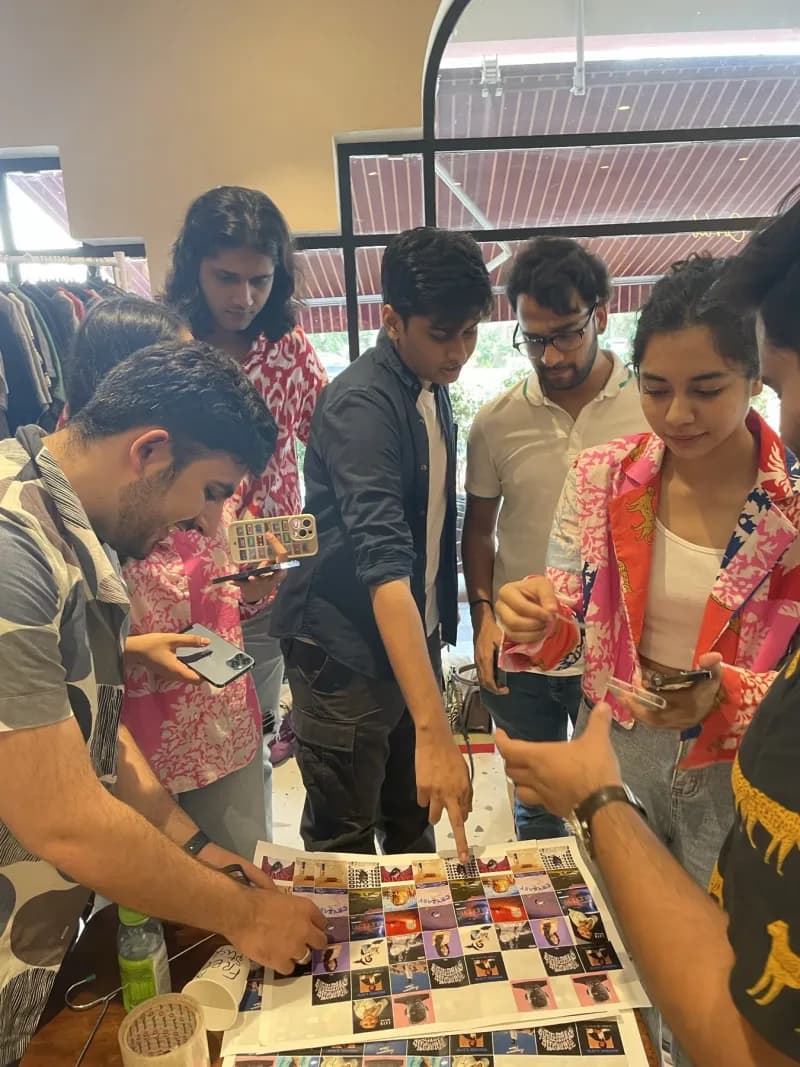 A group of friends huddled around a table of art prints and stickers at a cafe edition, phones out, picking through the sheets together.