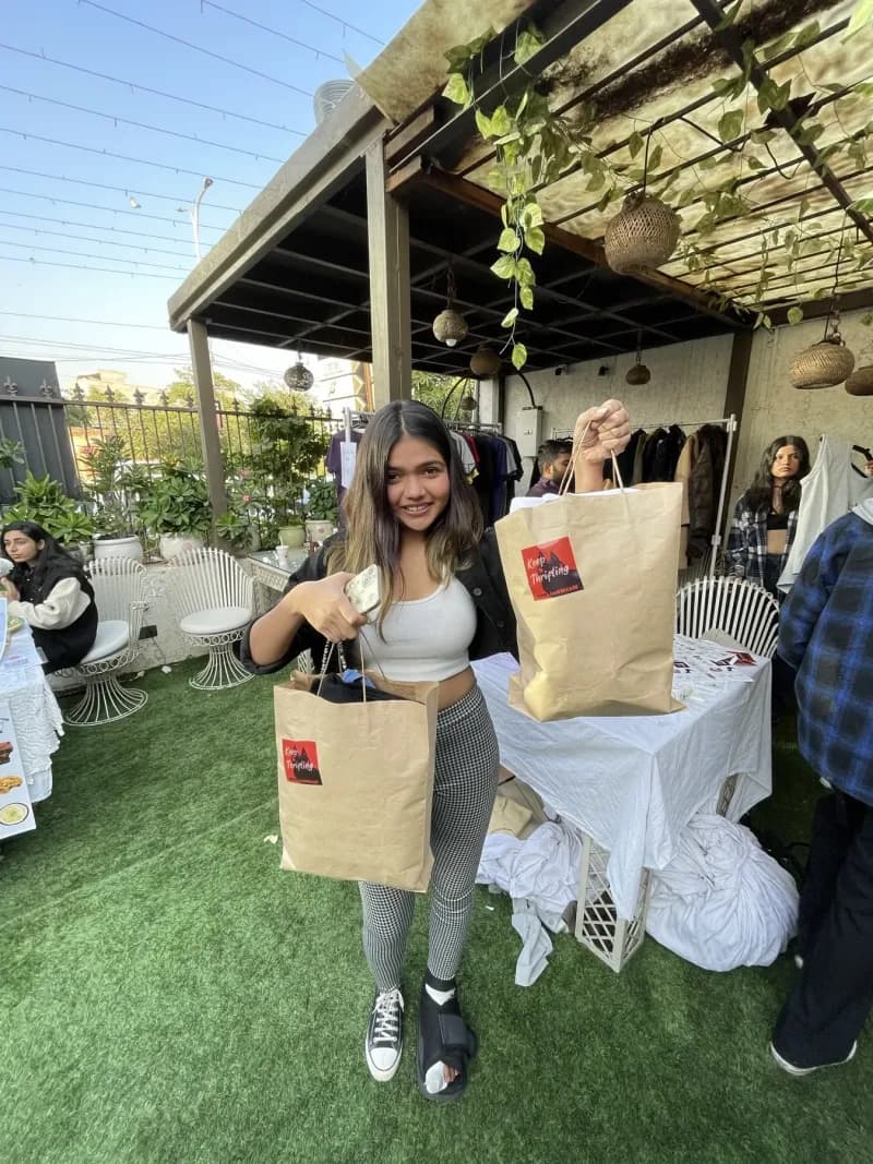 A guest holding up two full "Keep Thrifting" haul bags on the lawn at an outdoor edition.
