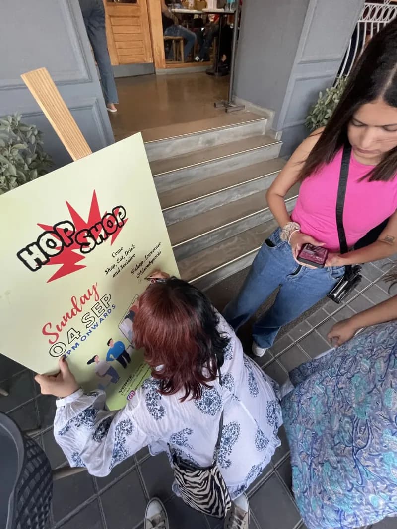 A hand-lettered HopShop poster reading "Come shop, eat, drink and socialise", propped up outside the cafe on the day of an early edition.